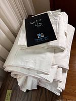 Stack of folded white linen fabric sheets with a label 'Lot #42' on top, showing size and texture details.