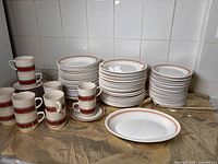 Stacked dishes show dinner plates, bowls, and side plates with Oxford pattern; cups and saucers with brown stripes placed on the side.
