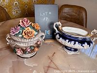 Both ornate decorative ceramic items, one with lid and multicolored roses, displayed on a table.