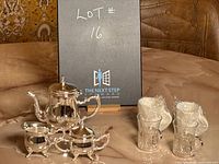 Photo showing the metal espresso set with mini coffee pot, creamer, sugar bowl, and 4 glass cups, all displayed on a marble table surface with a card in the background.