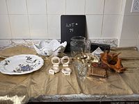 Wide photo showing entire lot of various kitchen and entertainment items on gold cloth with tiled backsplash