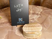 Closed shell-shaped mother of pearl jewelry box next to a sign showing lot number 25 on a polished marble surface