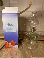 Oil lamp with original box showing floral design and brand Casa, positioned next to the lamp with glass chimney and green tint reservoir.