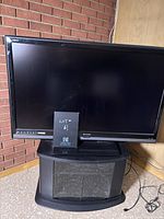 Sharp flat-screen TV sitting on a black swivel stand with frosted glass cabinet doors in front of a brick wall.