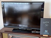 Front view of Toshiba television on stand with remote control beside it on a wooden cabinet.