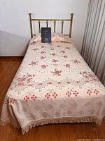 Full view of vintage brass single bed frame with floral bedspread shown for scale and styling. Headboard and rails visible.