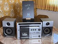 Photo of vintage audio system set consisting of receiver, cassette tape deck, and two speakers on a table with patterned wall in the background.