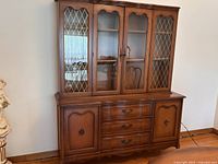 Front view of vintage two-piece china cabinet showing glass doors on top section and wood doors with drawers on bottom section.