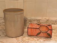 Photo showing vintage ceramic crock and stained glass look tissue holder side by side on a countertop with tiled backsplash.