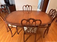 Full view of dining table with six chairs in a fruitwood finish on wood floor.