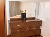 Front view of vintage wood dresser with attached mirror showing four drawers and mirror reflecting bed and curtain.