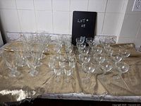 Photo showing vintage drink glasses in various sizes, patterns, and functions arranged on a cloth with a blackboard labeled Lot # 68.
