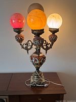 Full front view of lamp on tabletop showing base, arms and three lit globes