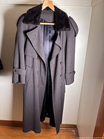 Front full view of vintage dark maxi wool coat with faux fur collar and belt hung on wooden hanger
