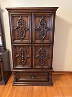 Closed view of wardrobe showing four ornately carved doors and a bottom drawer