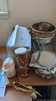 Photo showing woven basket with nested ceramic bowls, shells inside bowl, salt lamp, dreamcatcher drum, mirror, and garden greenhouse parts on a table.