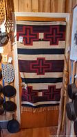 Wool blanket hung on a door showing full blanket with cross pattern and fringes at bottom.
