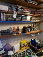 Shelf with Buddha bookends, lion bookends, Cortez figure, bowls, and various objects including CDs and computer keyboard.