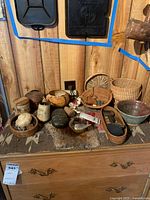 Photo showing several woven baskets, ceramic and metal bowls, a leather match holder, and various small decorative items arranged on a wooden surface.