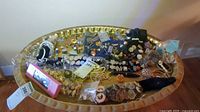 Wide view of varied costume jewelry laid on a large gold-tone tray showing numerous items including earrings, pins, bracelets, and necklaces.