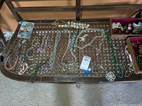 Overview of multiple necklaces laid out on a metal mesh table surface, showing various bead types and colors