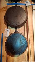 Two Erie fry pans hanging on wood slats, underside view showing “ERIE” stamp and size numbers 8 and 7.