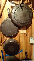 Three cast iron skillets (Griswold No. 7, Griswold No. 8, HFCo 8&9) hung on wooden wall.