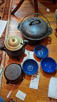 Overview photo showing Griswold Tite-Top Dutch Oven, brass kettle, three blue metal bowls, and smaller cast iron pot on wooden floor.