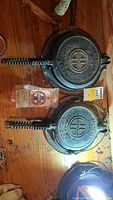 Two cast iron waffle irons side by side with coil handles and a Griswold tag
