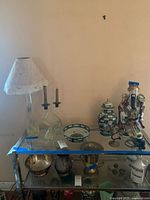 Full lot showing glass base lamp with paper-like shade, two clear glass candlesticks, Asian-inspired ceramic bowl and urn, brass dragon bell, and the 18-inch colorful figurine.