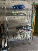 Front view of adjustable six shelf metal wire shelving unit with contents on shelves, contents not included in sale. Shows structure and height of unit against wall with golf clubs nearby.