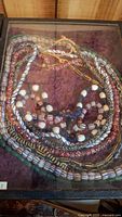 Overhead image of multiple strands of Indigenous American beaded necklaces in a display case with purple velvet backing.