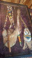 Full view of necklace, pipe, fur pouch, feather, and beaded pouch inside glass display case