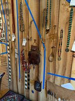 Beaded necklaces hanging on a wooden wall with double-handled wooden spoons, leather pouch bag, and a leather framed mirror also visible.