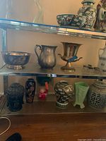 Top and middle shelf overview showing silver plated serve pieces, ceramic jars, small glass containers and decorative vases