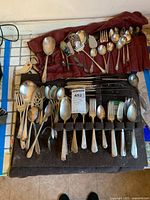 Wide shot of the full collection of silver plated and sterling flatware and serving pieces laid out on black felt roll and red cloth.