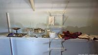 Photo shows a variety of trays, containers, vintage fans, scarves, and handkerchiefs arranged on white wire shelves.
