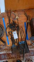 Full collection showing various fireplace tools including shovels, pokers, tongs, and a metal chain arranged on a wooden floor