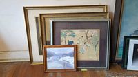 Group photo of five framed prints of varying sizes and designs. Includes a small snow landscape painting in wood frame and other larger prints with gold and silver frames.