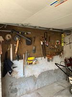 Wide view of pegboard wall with various hand tools and hardware hung on hooks, showing saws, levels, clamps, tape measures, goggles and more