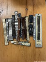 15 assorted watch wristbands laid out on wooden surface, various materials, colors and styles distinctly visible