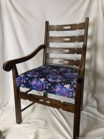 Front view of dark wooden armchair with blue and purple floral patterned upholstered seat and horizontal slatted backrest with cut-out accents.