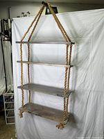 Front view of the hanging wooden shelf unit showing four shelves supported by thick ropes and adjustable dowels.
