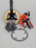 Photo showing black crank arm with gold and silver chainrings, orange cable lock, black multi-tool, black folding lock, and small lubricant vial.