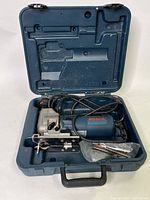 Open hard plastic carrying case containing Bosch jigsaw, power cord coiled, and a bag of extra saw blades.