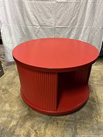 Full view of the round red coffee table showing the solid top and tambour door closed.