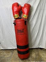 Full view of red Everlast punching bag with gloves hanging above, showing bag height and wear.
