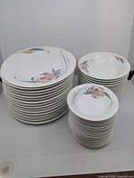 Stack of 15 large dining plates, 15 side bowls, and 13 salad/soup bowls arranged in three piles showing quantity and floral pattern