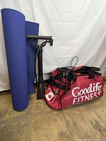 Blue yoga mat rolled up beside a black air pump and a red GoodLife Fitness gym bag