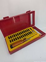 Open red plastic case showing screwdriver with transparent orange handle and yellow bit tray with various bits inside.